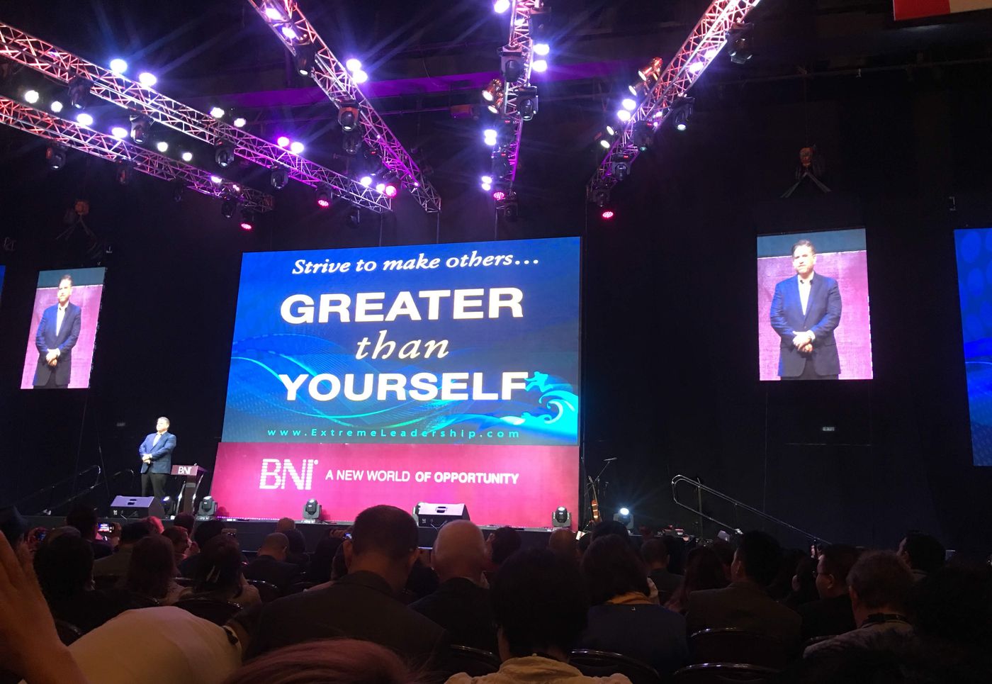 Sân khấu hội nghị doanh nghiệp toàn cầu tại Thái Lan năm 2018, màn hình lớn ghi Strive to make others greater than yourself